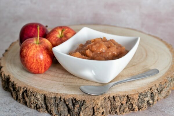 bowl of gala chunky applesauce on a rustic wooden slab with three apples and a silver spoon