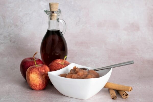 gala chunky cinnamon and maple syrup apple sauce in a bowl with cinnamon sticks, maple syrup and apples in the background