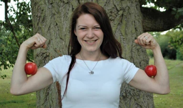 attractive fit young woman with an apple on each bicep smiling at the camera in front of an impressive tree is applesauce as healthy as an apple