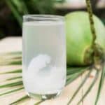 A glass of coconut water on a table with a coconut