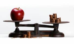Picture of a apple and coins on a balance scale to illustrate what effects food prices from the tree of knowledge